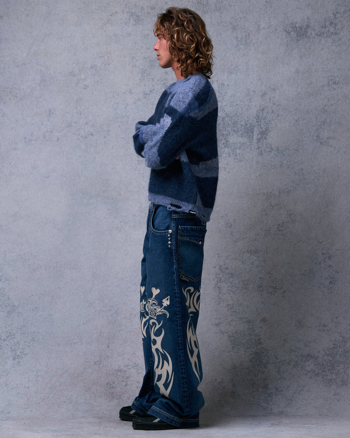 Model wearing the dark stone wide-leg jeans in side profile, showing the studded pocket, full leg width and tribal graphics