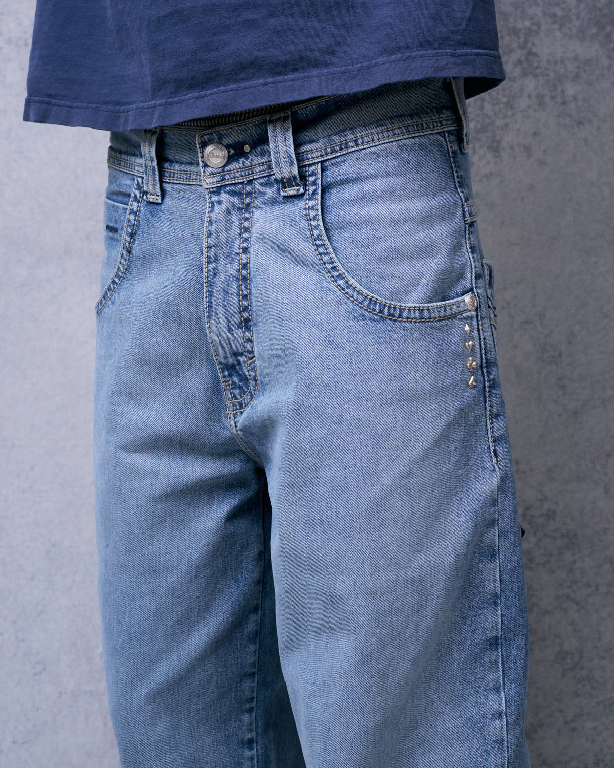 Front of light blue wide-leg jeans on a model, showing button fly area and card-suit studs below the coin pocket