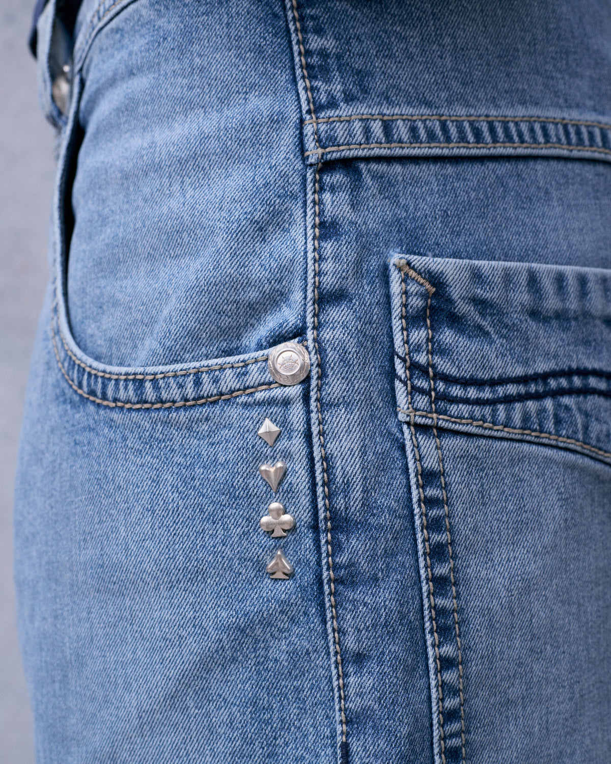 Close-up of diamond, heart, club and spade metal studs beside the front pocket of light blue jeans