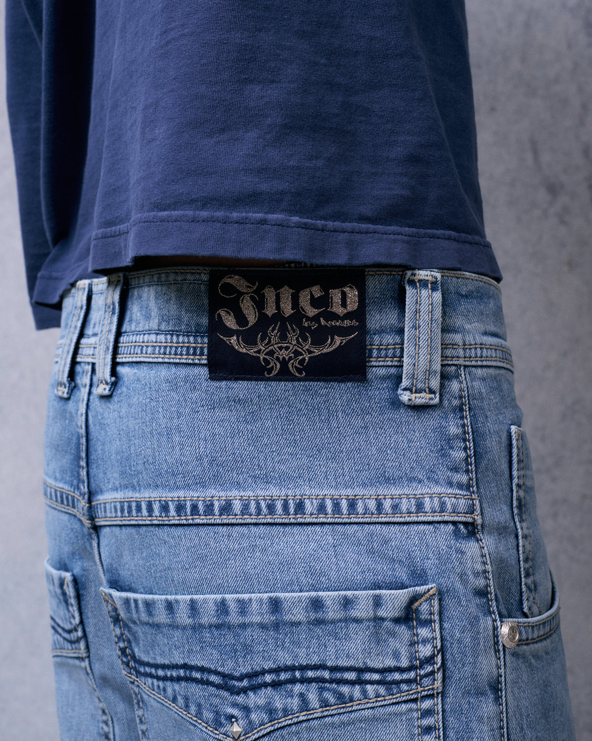 Black JNCO Los Angeles tribal label on the back waistband of light blue jeans, close-up
