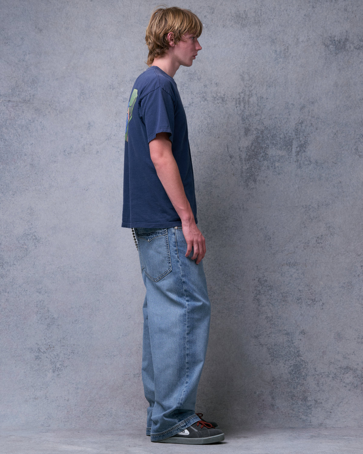 Model wearing light blue wide-leg jeans with a wallet chain and grey sneakers, side view