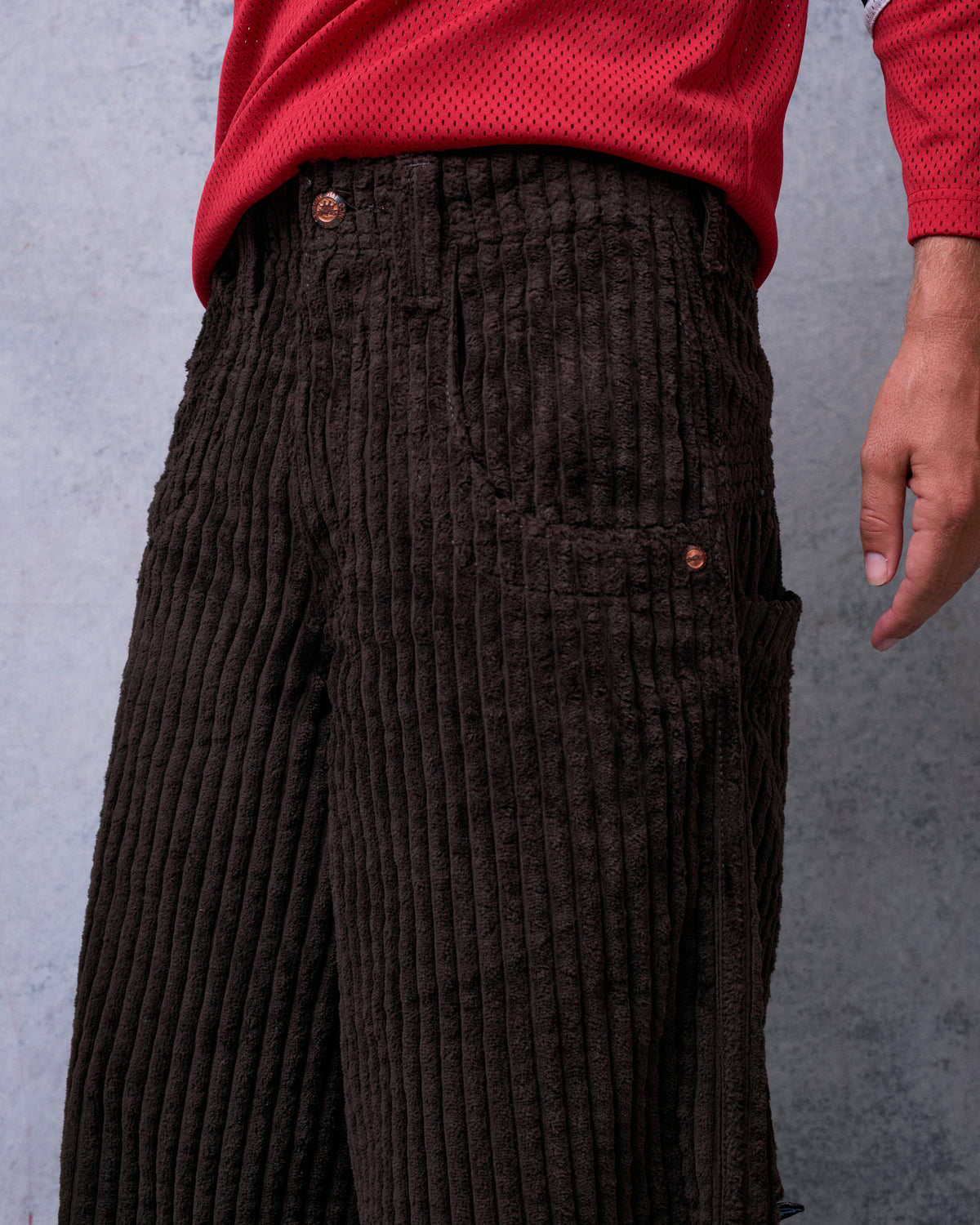 Close-up of brown wide-leg corduroy pants on a model, front pocket area with copper rivets and side pocket