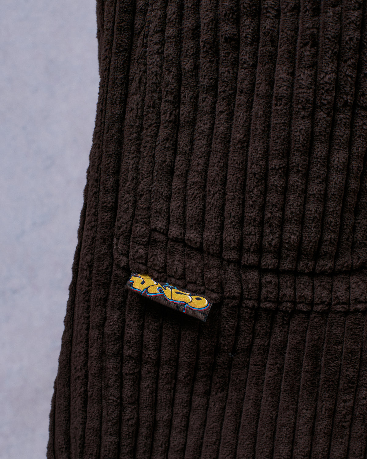 Close-up of brown wide-wale corduroy at the leg with a yellow graffiti-style JNCO woven tab sewn into a seam