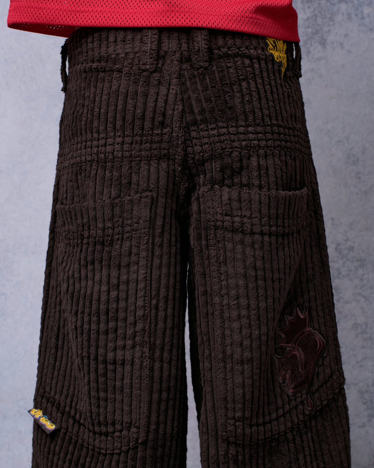 Model wearing brown wide-leg corduroy pants, back view showing pockets, waist patch, tonal crown J patch and JNCO tab