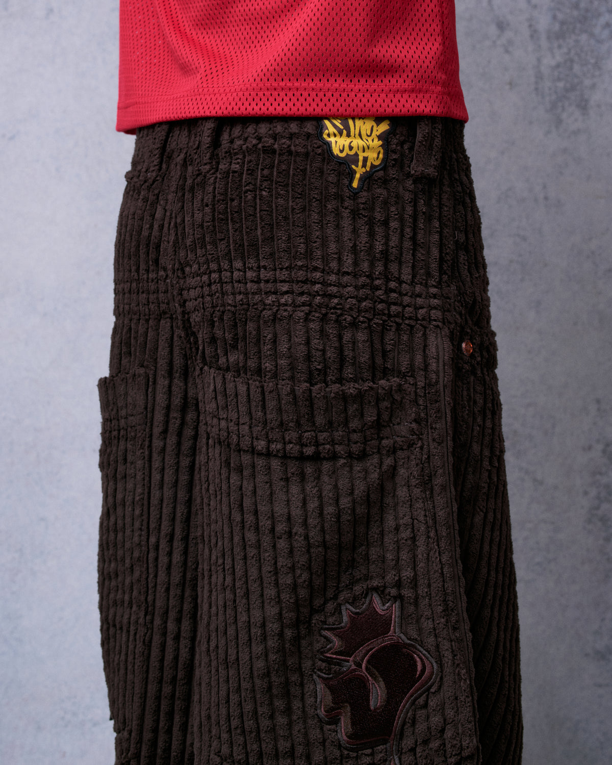 Model wearing brown corduroy pants, angled back view of the back pocket, yellow waistband patch and tonal crown J patch