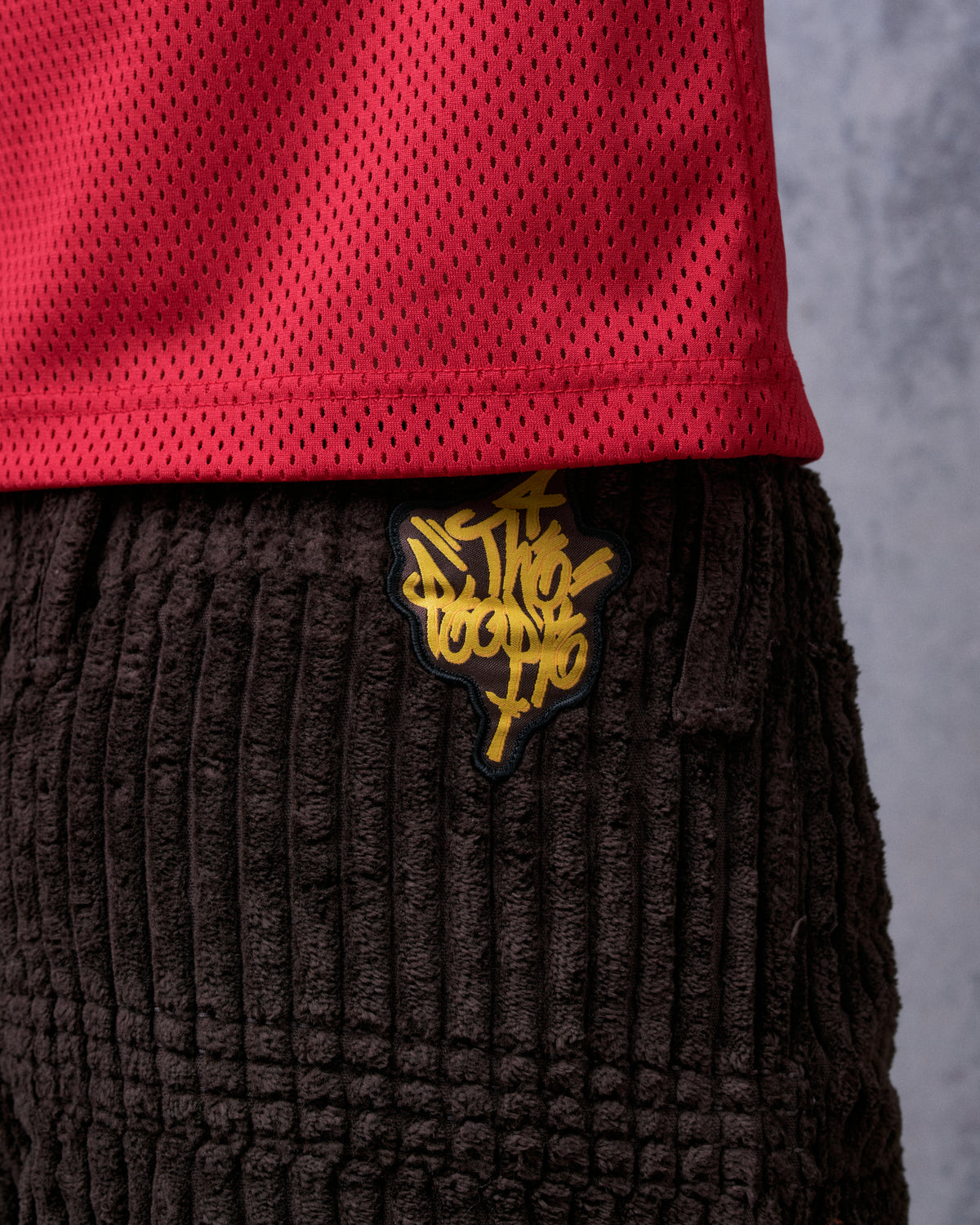 Close-up of a yellow graffiti 4 The People patch on the brown corduroy waistband below a red mesh top