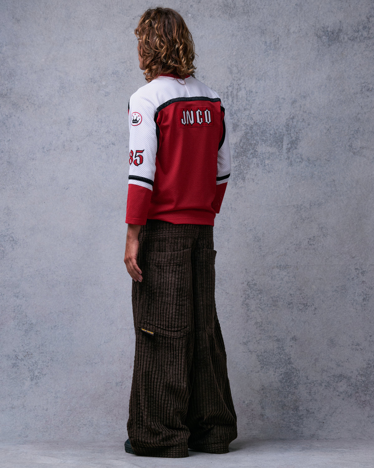 Model wearing brown wide-leg corduroy pants, back view from the other side showing a back pocket and yellow side tab