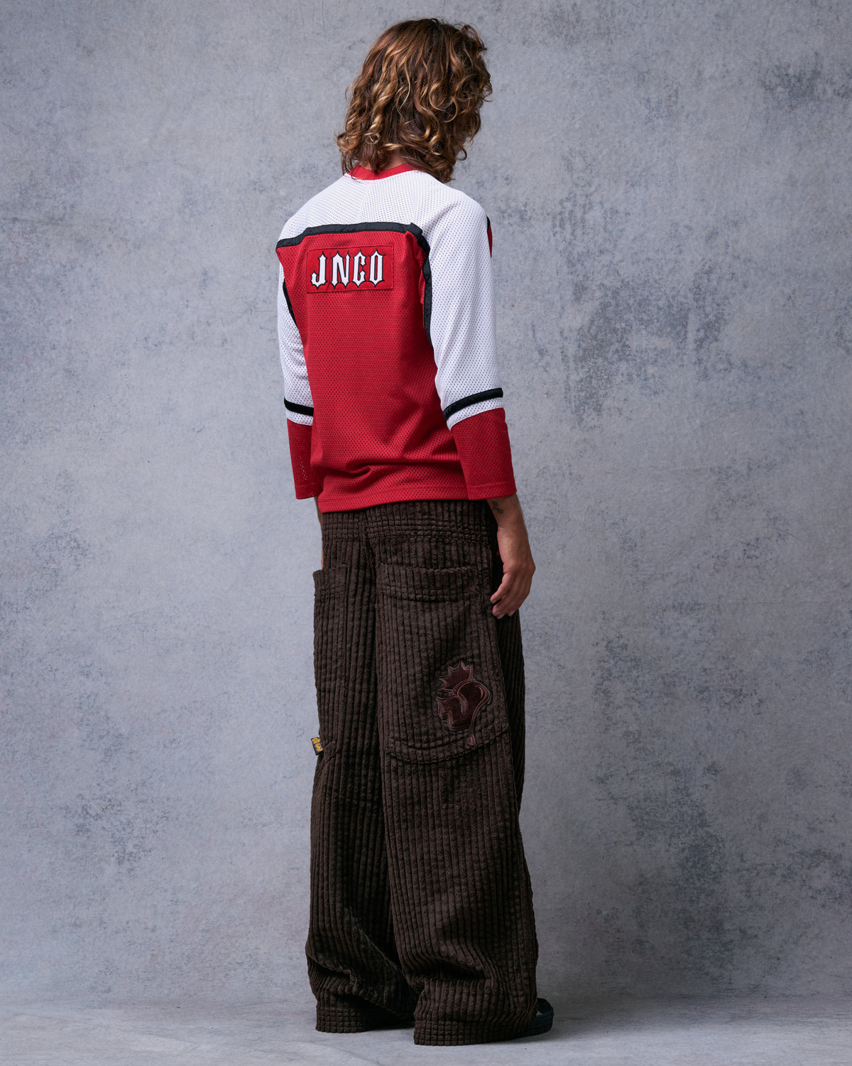Model wearing brown wide-leg corduroy pants, back three-quarter view showing back pocket with tonal crowned J embroidery