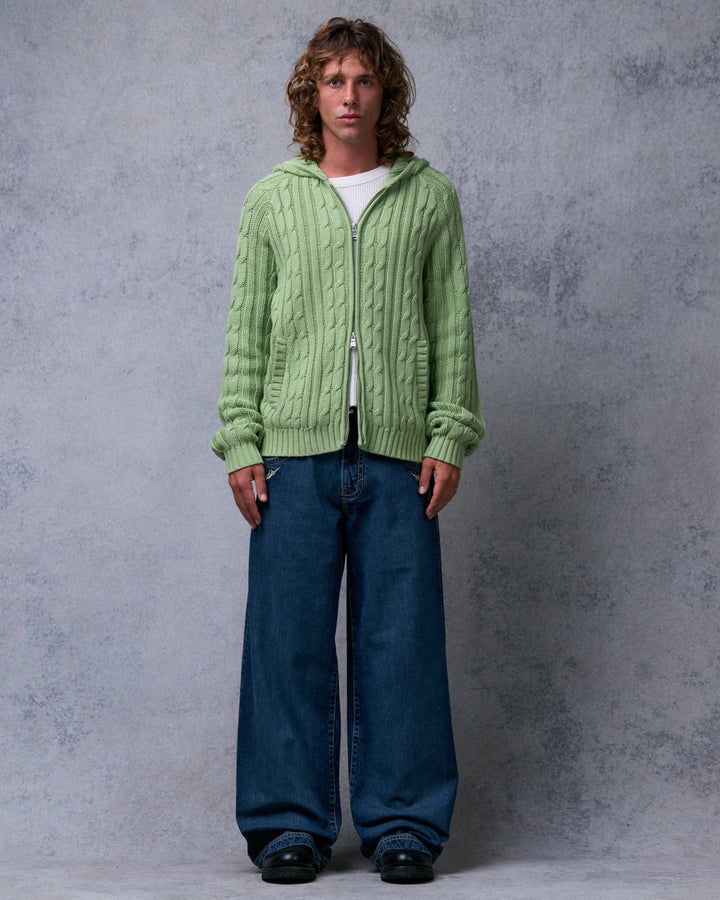 Model wearing dark stone wash wide-leg jeans with a green cable-knit hoodie, front view, arms at sides