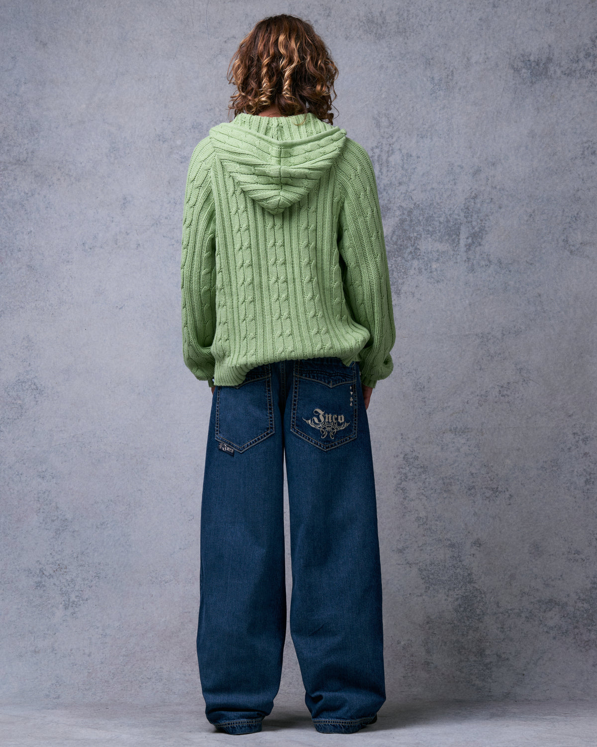 Model wearing dark stone wide-leg jeans, back view showing embroidered JNCO tribal logo on one back pocket