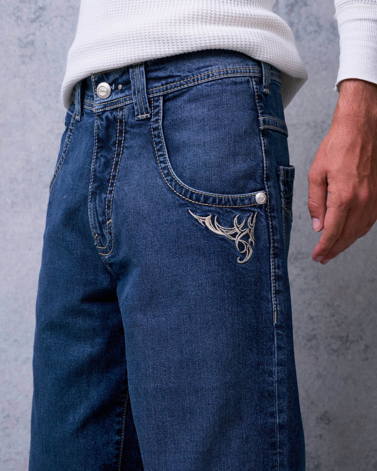 Close-up of the dark stone jeans' front, showing contrast stitching, button fly and tribal embroidery below the pocket