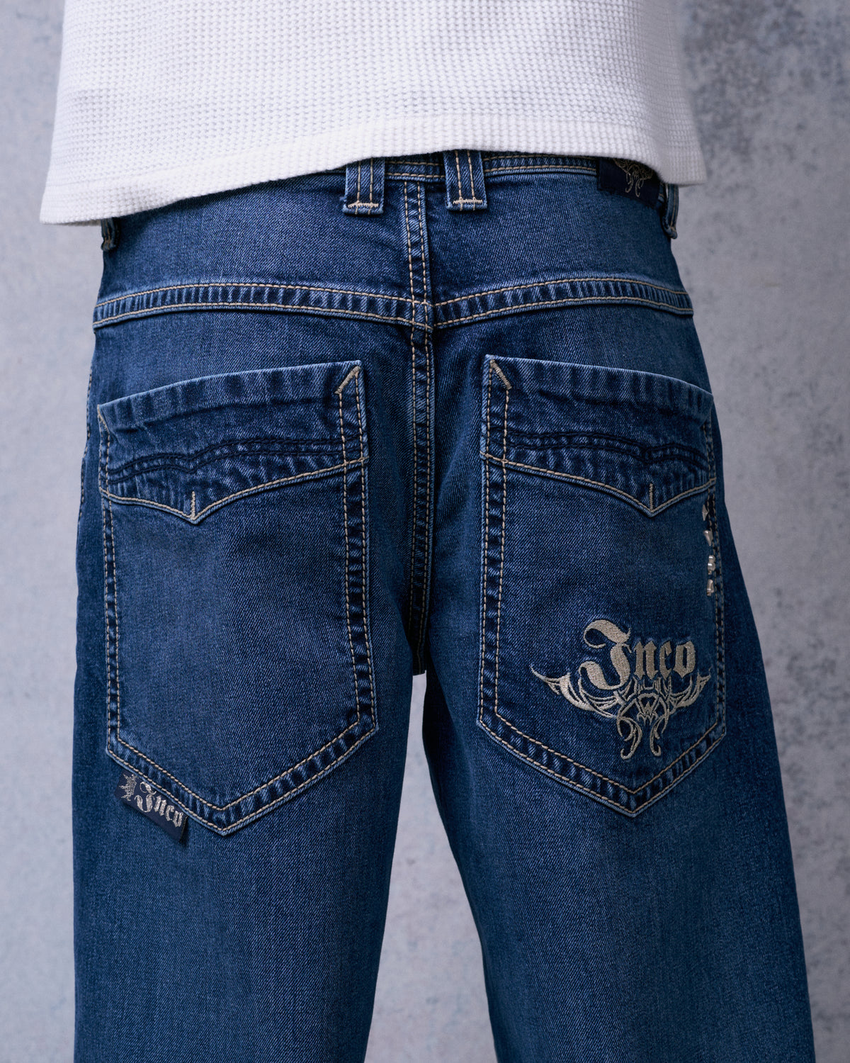 Straight-on back view of dark stone wash jeans with JNCO tribal embroidery on one back pocket