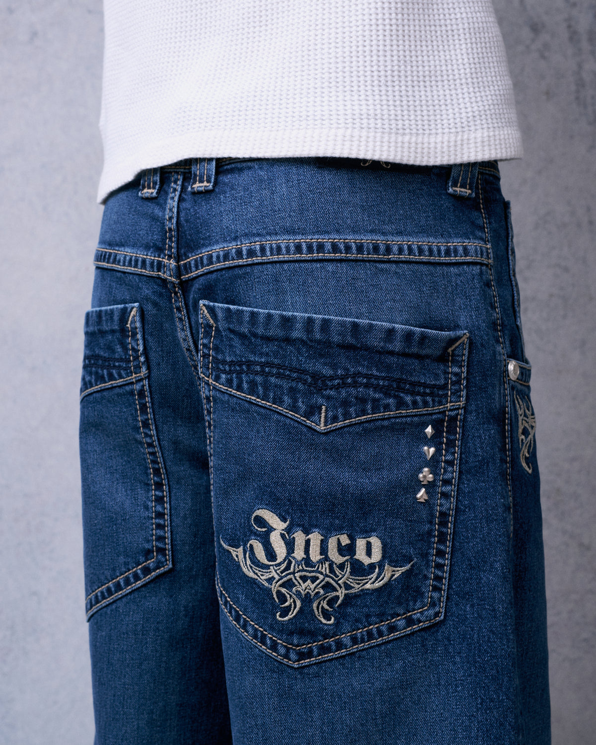 Close-up of a back pocket with pale metallic JNCO tribal embroidery and four card-suit rivets