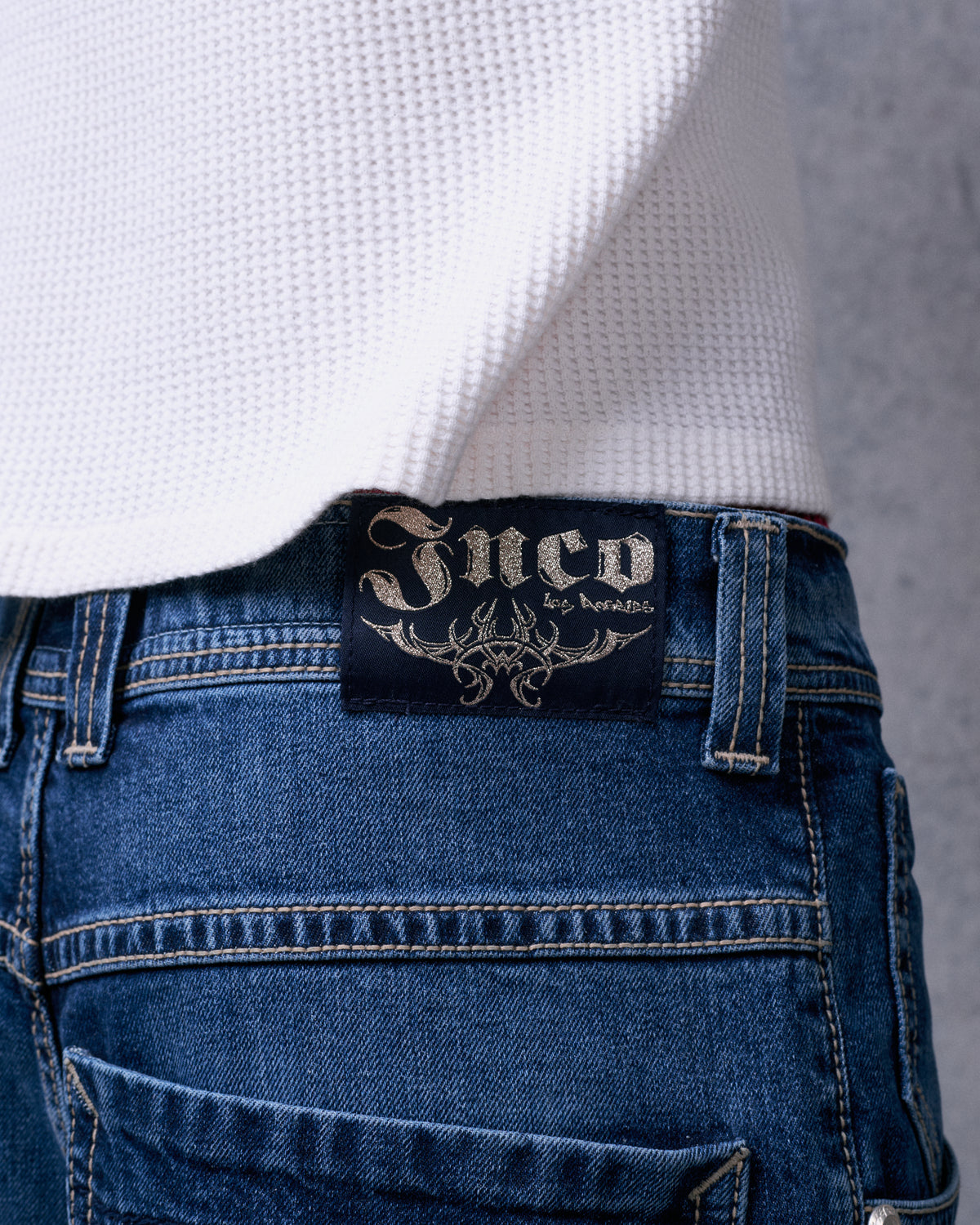Close-up of the black JNCO Los Angeles waistband label with metallic tribal design on dark stone denim