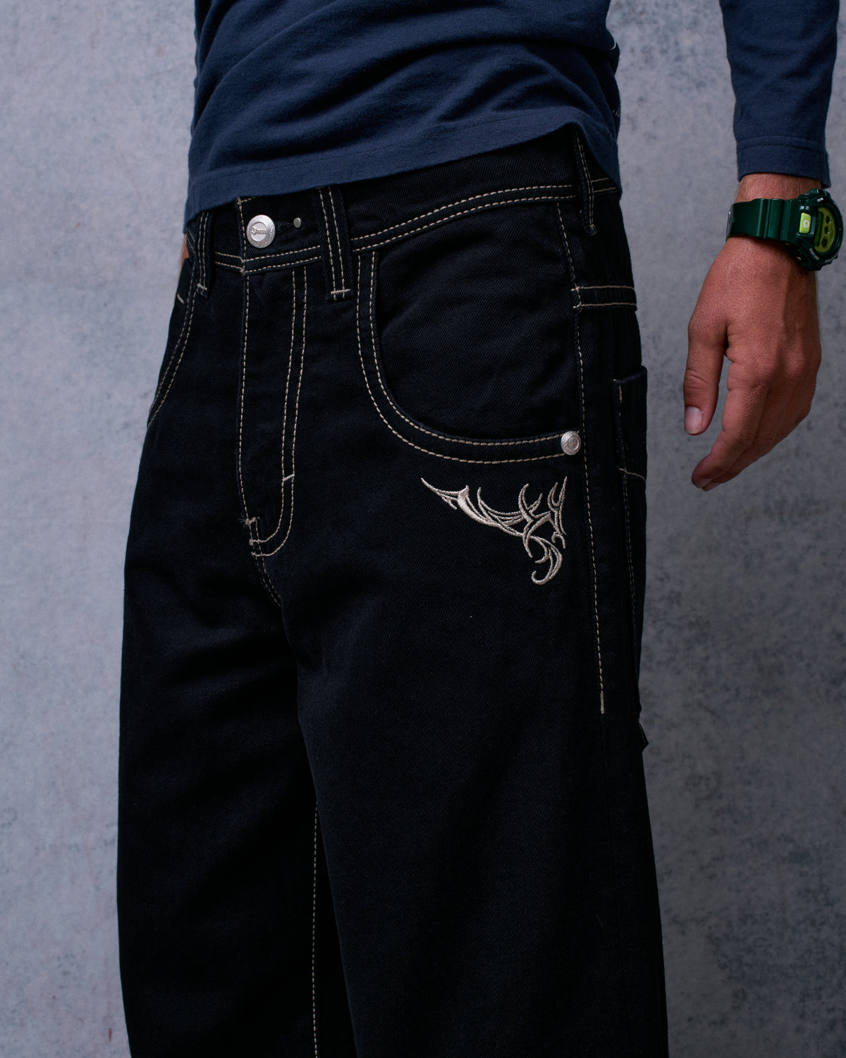 Model wearing the black wide-leg jeans with a navy top, front close-up of the waist and tribal embroidery by the pocket