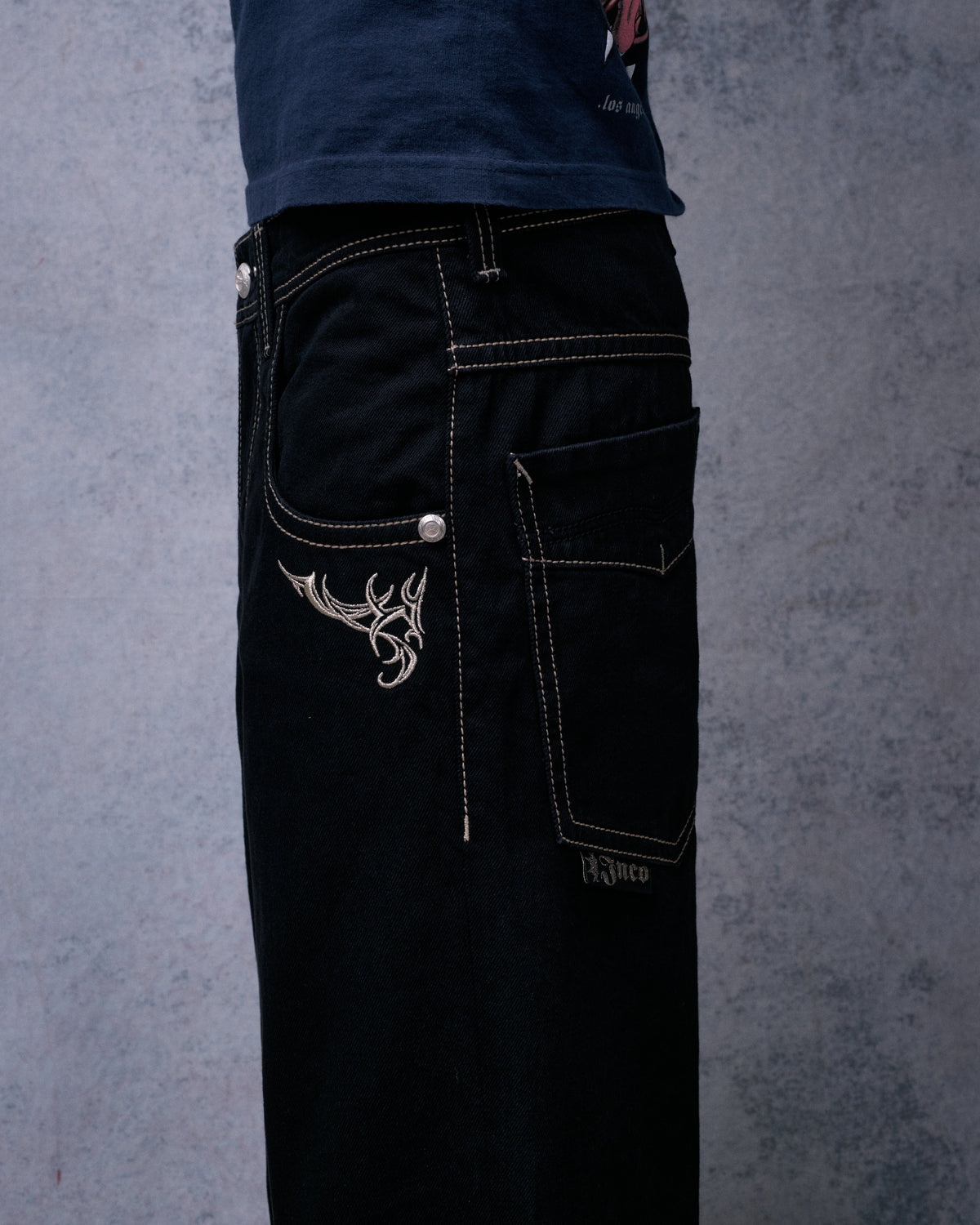 Model wearing the black wide-leg jeans, side view showing front tribal embroidery, back pocket and Jnco tab