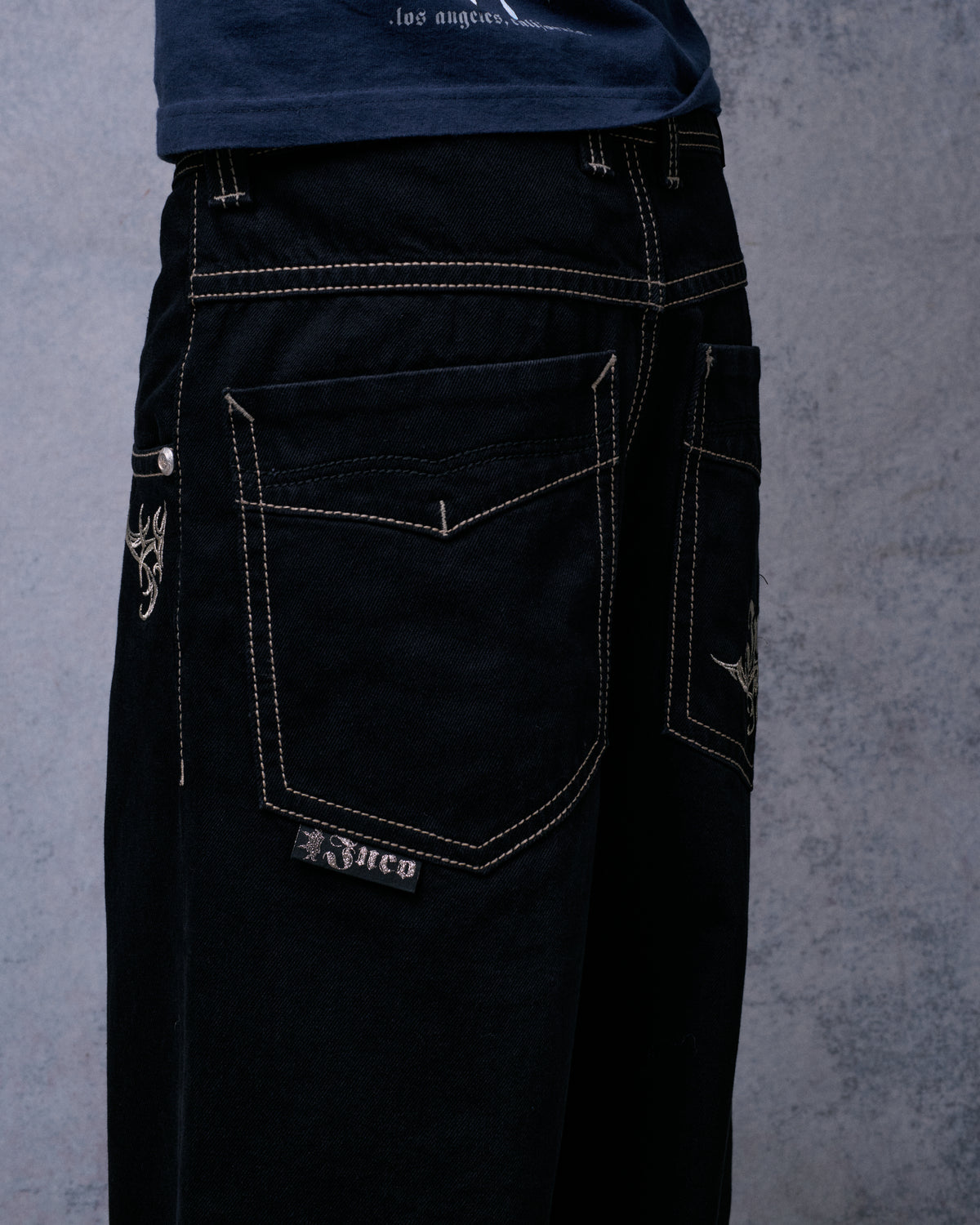 Model wearing the black wide-leg jeans, rear three-quarter view of a plain back pocket with Jnco tab