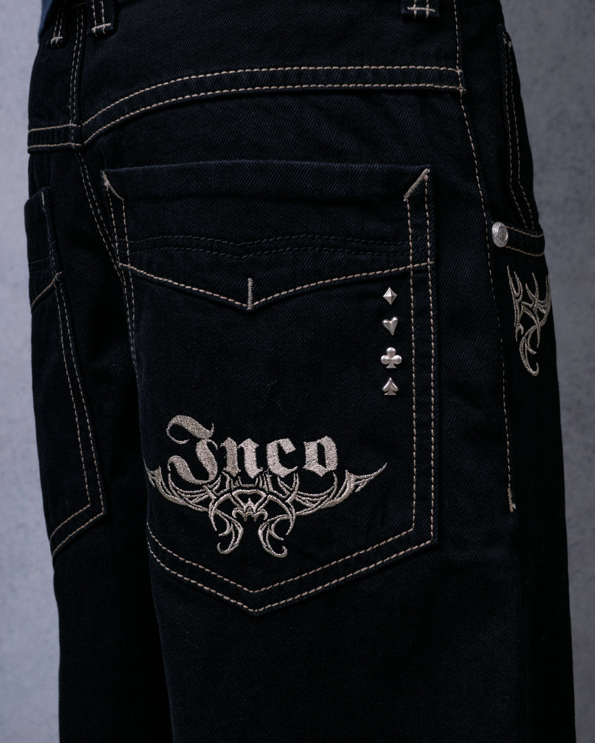 Close-up of the back pocket with Jnco tribal embroidery and four card-suit rivets: diamond, heart, club, spade