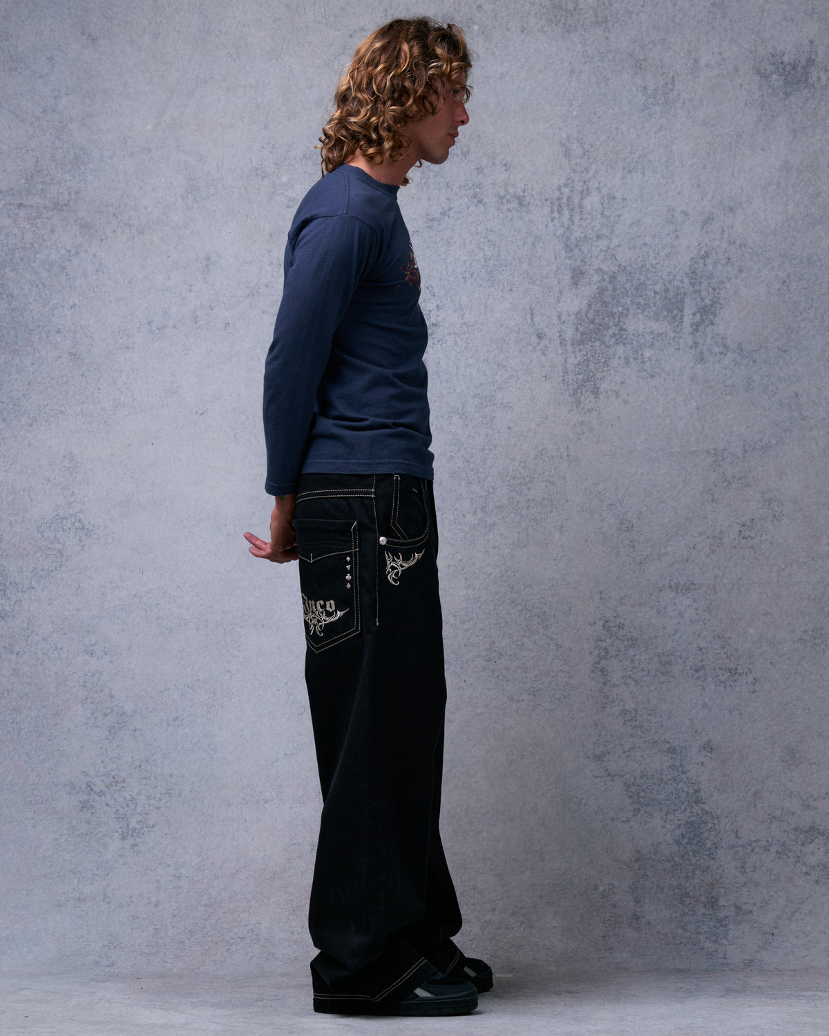 Model wearing black wide-leg jeans, right side profile, showing back pocket and front corner embroidery