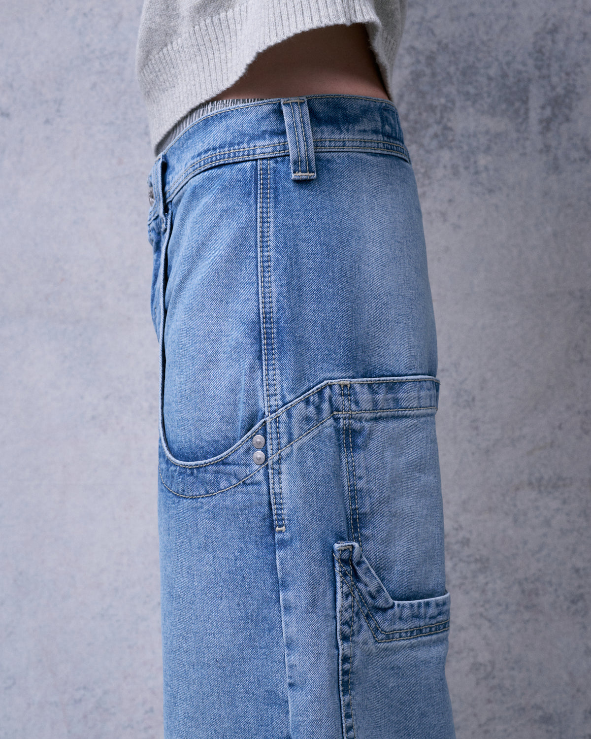 Close-up side view of the jeans hip showing contrast stitching, rivets and a back pocket