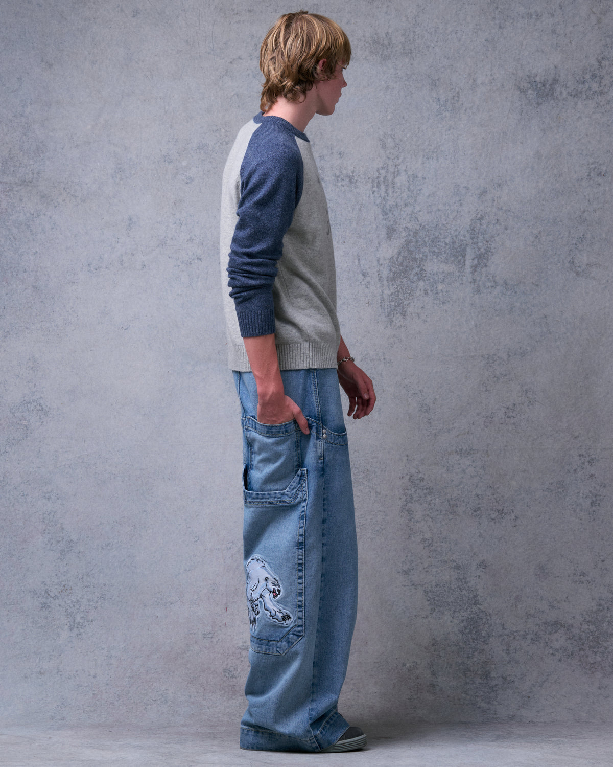 Model in side view with a hand in the back pocket, showing the polar bear patch on the oversized lower pocket